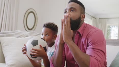 Happy-african-american-father-and-son-watching-football-match-and-supporting,-in-slow-motion