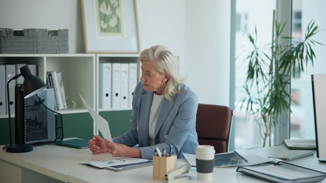 Ældre forretningskvinde arbejder med dokumenter ved sit kontorbord.