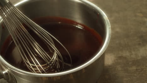 closeup metal whisk putting into melted chocolate in slow motion.