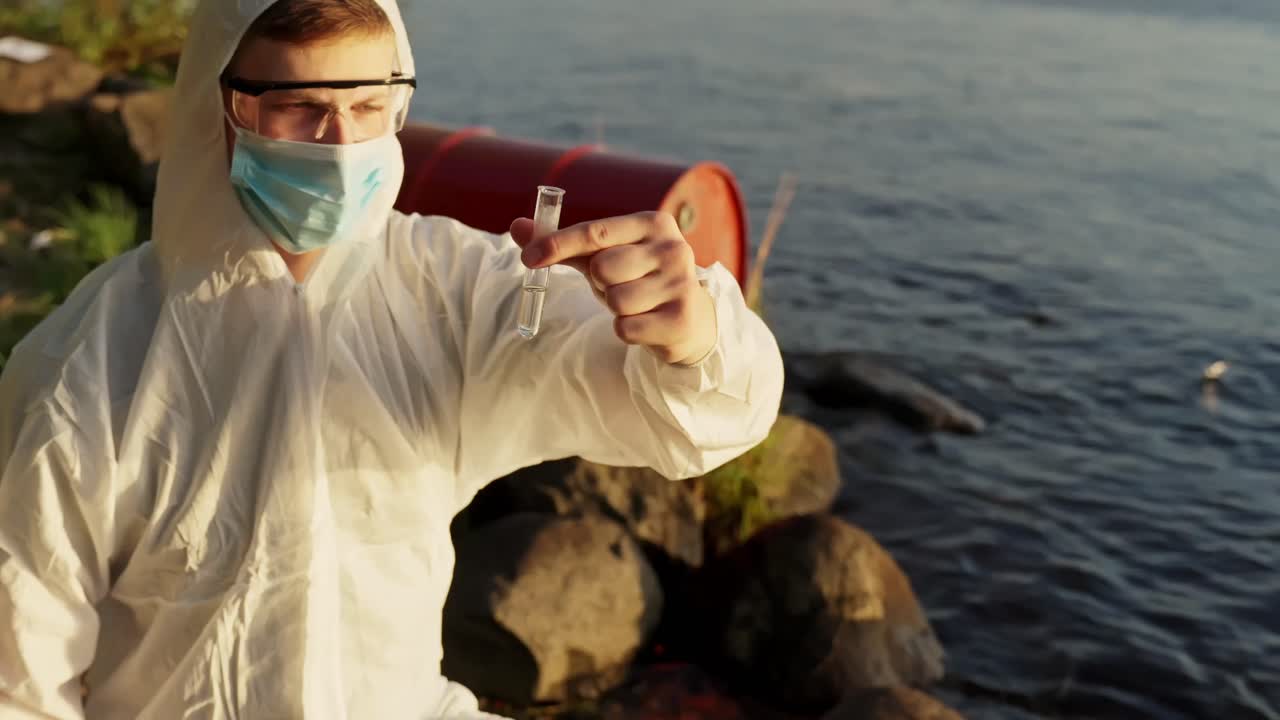 Um inspetor vestindo um traje de materiais perigosos segura ferramentas de teste perto do lago enquanto examina os níveis de poluição perto da costa
