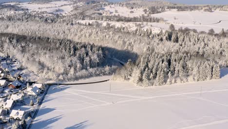 Vuelo-De-Drones-Sobre-Un-Paisaje-Invernal-Con-Un-Pequeño-Pueblo-A-La-Izquierda,-Vuelo-Suave-Bajando-Lentamente