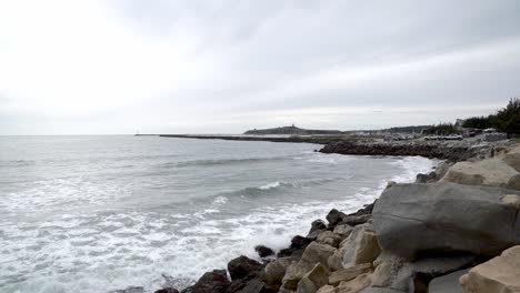 Far-away-view-of-a-jetty,-boats,-the-Pillar-Point-and-waves-crashing-onto-the-shore