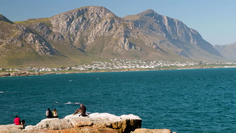 spectators on coastal rocks whale watching with beautiful mountain backdrop