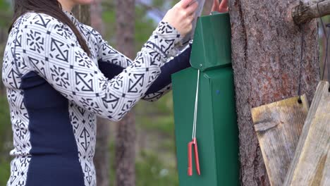 Female-hiker-removes-registration-book-from-metal-container-at-trailhead---Close-up