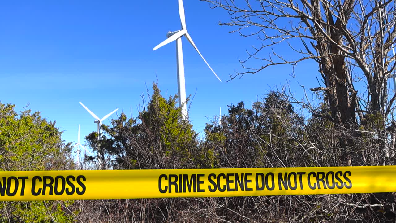 Gult politisperrebånd med teksten "åsted – ikke kryss" som svaier i vinden, med flere store vindturbiner som genererer ren, fornybar energi under en klar blå himmel i bakgrunnen
