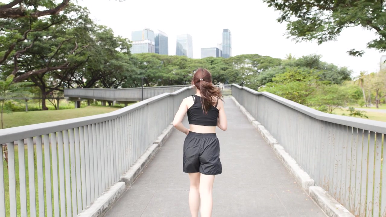 都市公園の橋を走る若い女性
