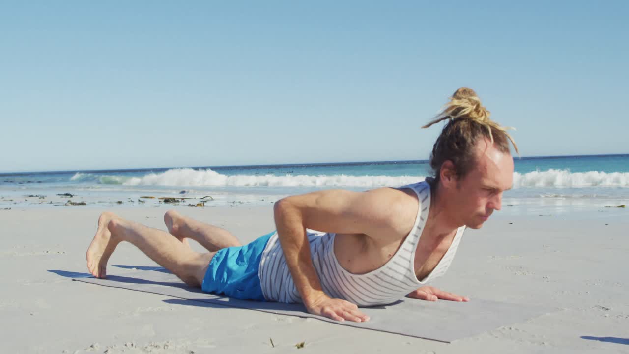 video de un hombre caucásico con rastas practicando yoga acostado en una playa soleada