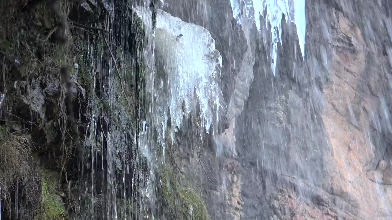Water Dripping Over Frozen Icicles on a Rocky Cliffside