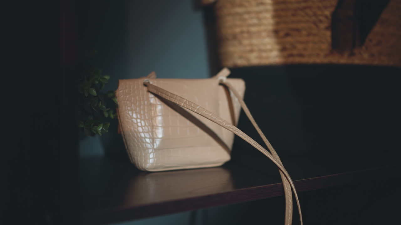 Una mano femminile appoggia una borsa da donna beige su una mensola nel corridoio.