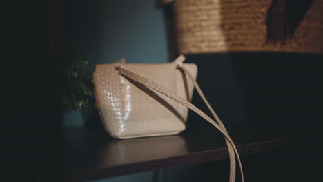 female hand puts beige ladies handbag on shelf in hallway