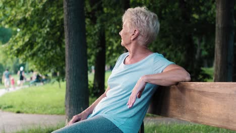 Senior-woman-sitting-on-the-bench-in-the-park-and-looking-around