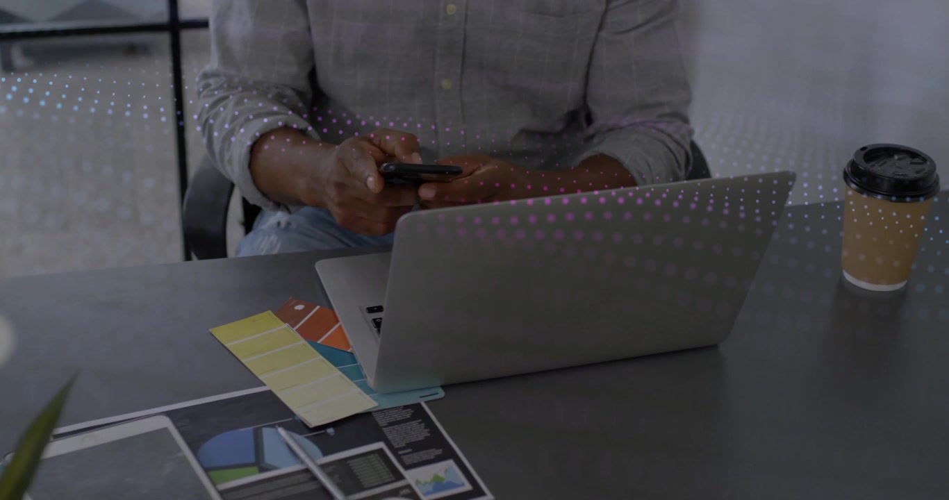 Designer reaching for charts then grabbing smartphone and reviewing designs while sipping coffee