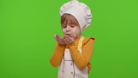 Child-girl-kid-dressed-as-professional-cook-chef-blowing-flour-from-hands-into-camera-on-chroma-key