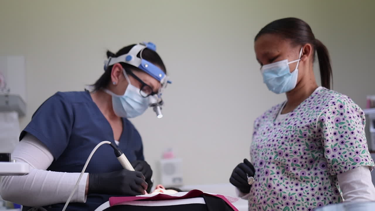 Dentist and assistant drill patient's teeth in dental chair, slo mo