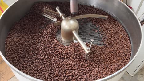 fresh specialty coffee beans resting on cooling and mixing tray to reduce the heat evenly after roasting, spinning in regular speed, production warehouse factory shot of food and beverage industry