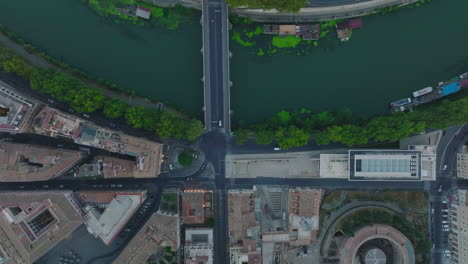 Top-down-panning-footage-of-buildings-and-streets-in-urban-borough-along-Tiber-river.-Tracking-of-car-passing-bridge.-Rome,-Italy