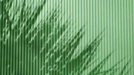 shadow of palm leaves on vertical green corrugated metal wall. abstract natural light and line pattern background. design for wallpaper, banner, postcard, greeting card, poster, vertical