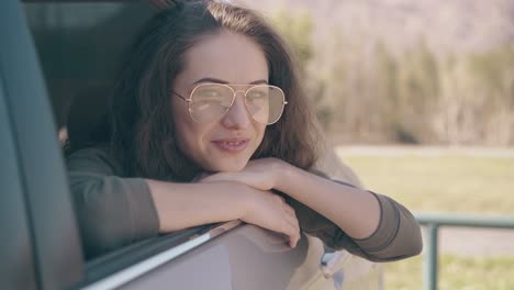 Una-Chica-Feliz-De-Pelo-Oscuro-Con-Gafas-De-Moda-Se-Sienta-Junto-A-La-Ventanilla-Del-Coche