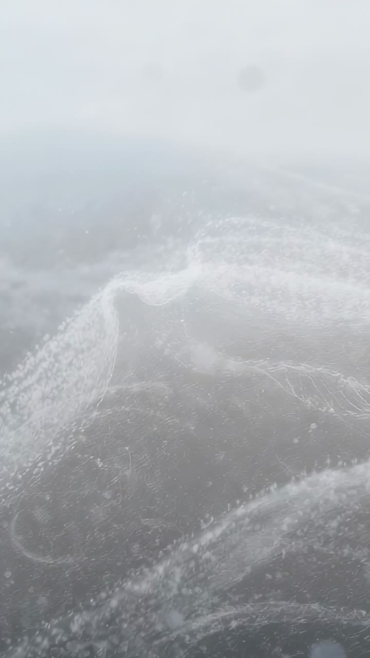 Vertical video: Shifting sea surface moving by current near misty horizon, with foam streaks