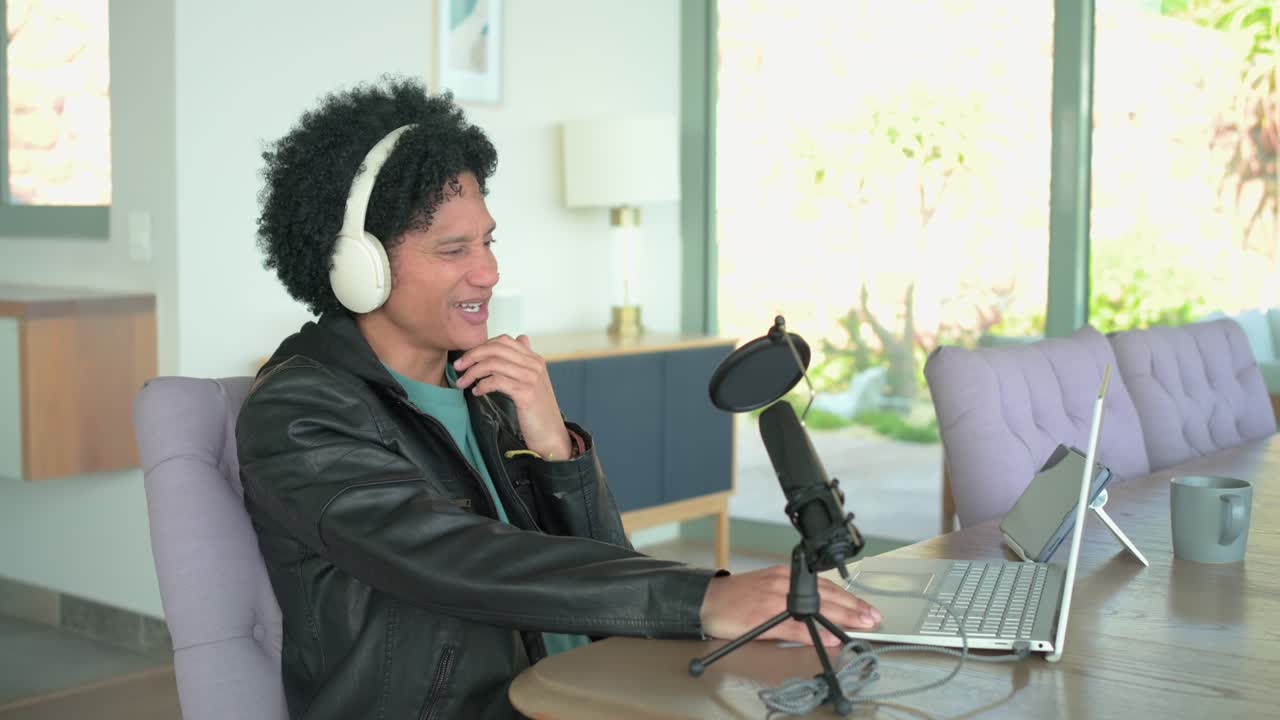 Man in his thirties entering office, donning headphones, using laptop and mic to record, copy space