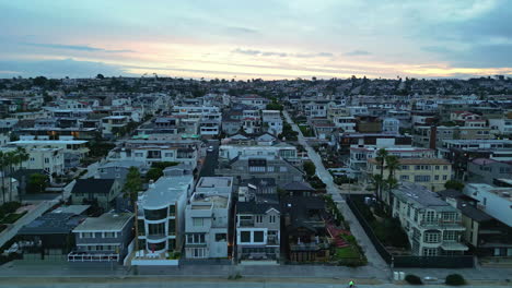 aerial drone pan shot over residential bungalows in city against blue sky along the beach of manhattan beach, california, usa during evening time