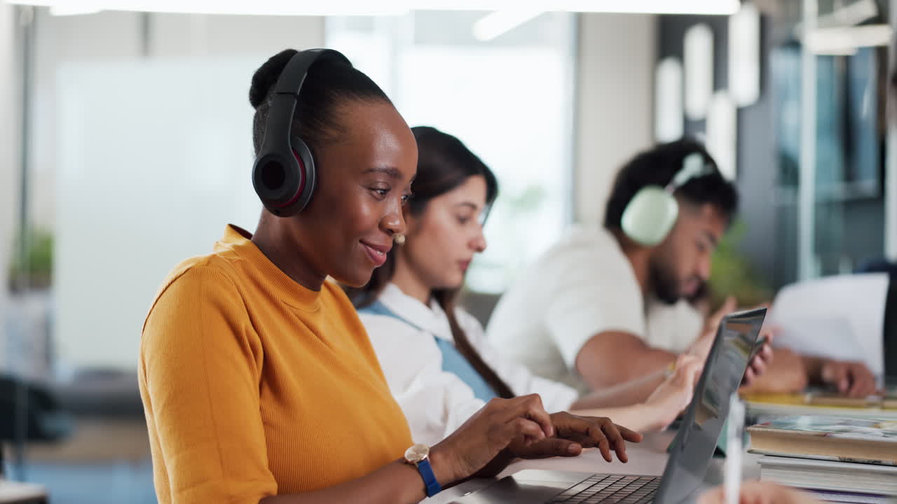 Young Black Woman Wearing Headphones and Typing on Laptop in Office