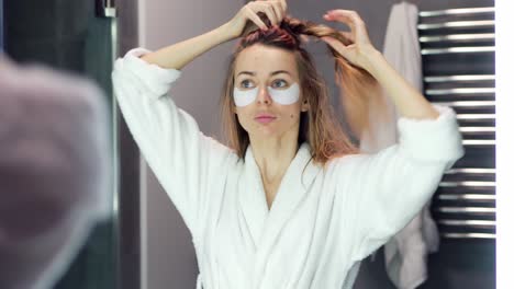 mujer de cabello rubio peina su cabello en el baño junto al espejo