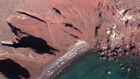 aerial spinning top view over red beach full of tourists and bathers, santorini