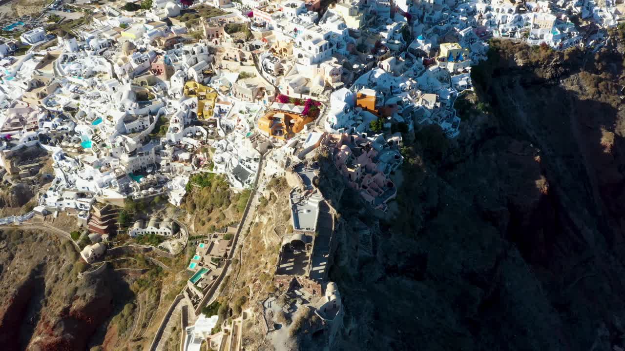 Drone flying towards famous village Oia with white cave houses and villas in Santorini, Greece.