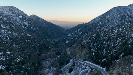 flight-thru-mountains-with-snow-road-to-the-right-with-cars-and-horizon-at-the-background-at-Ontario-CA