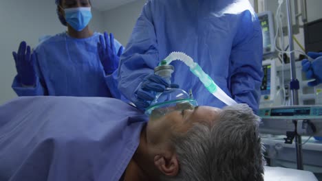Cirujanos-De-Raza-Mixta-Usando-Ropa-Protectora-Poniendo-Al-Paciente-A-Dormir-En-El-Quirófano