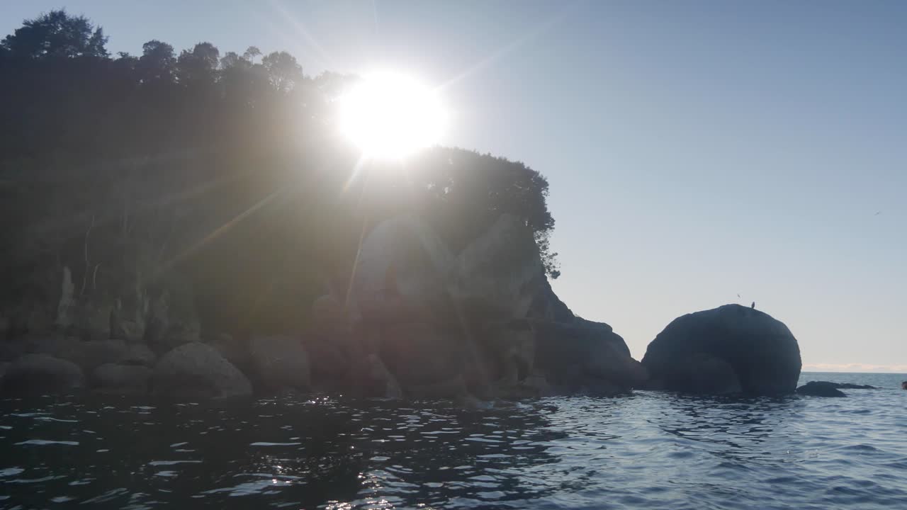 Sun ball burns bright onto NZ famous split apple rock seen from water