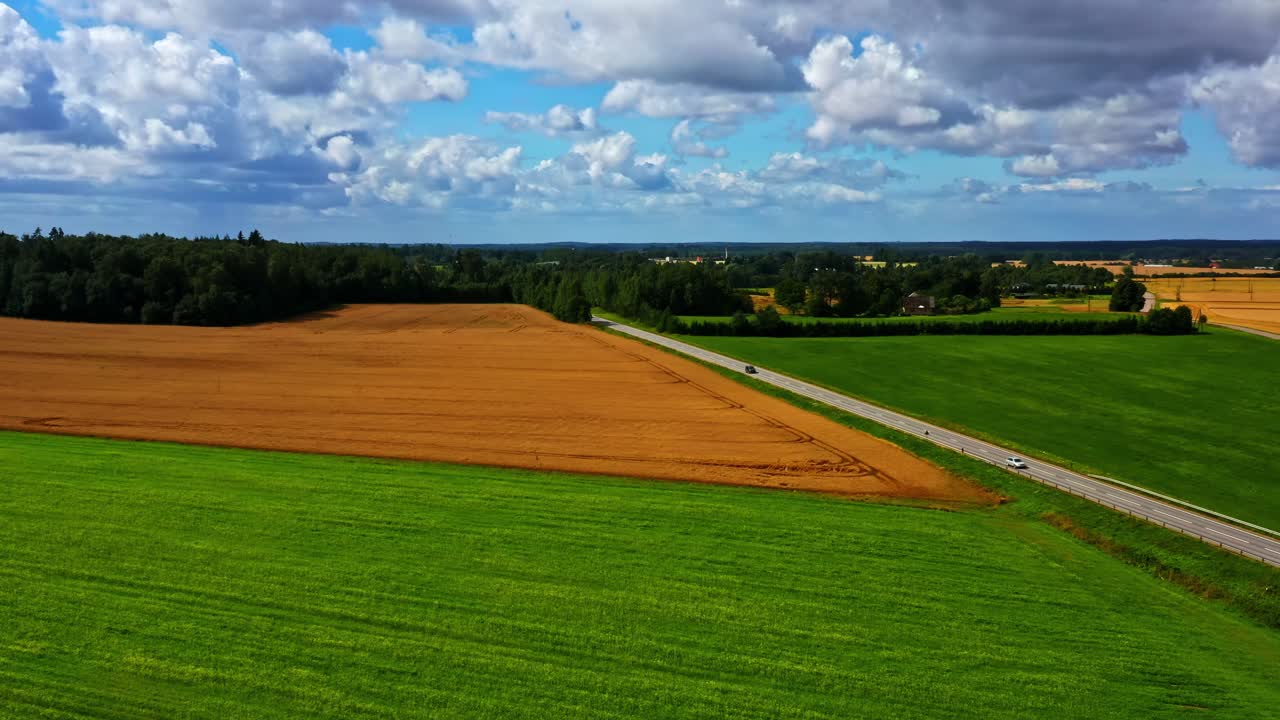 Aerial view of rural road dividing green and harvested fields under blue sky
