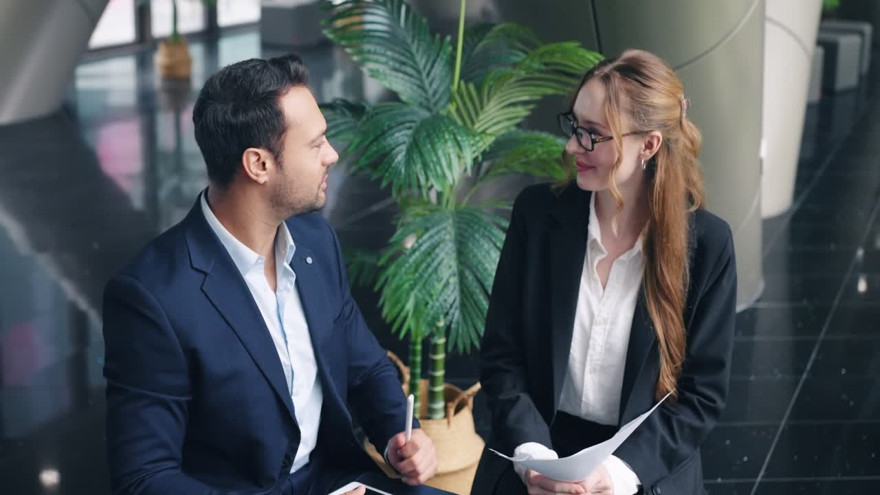 To glade, unge kollegaer fejrer et vellykket projekt eller en sejr med en highfive, mens de griner og smiler sammen på en moderne kontorgang og viser fantastisk teamwork.