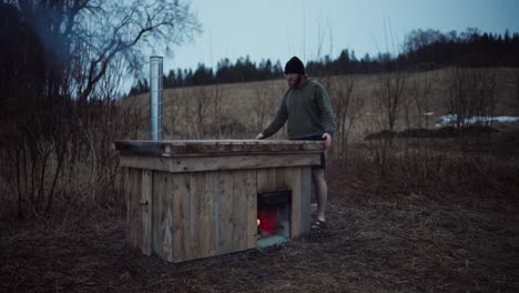 man removes the wooden cover of wood-fired hot tub