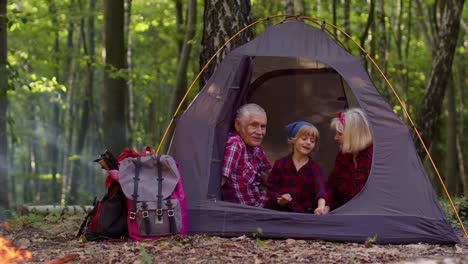 Senior-Großmutter-Großvater-Mit-Enkelin-Sitzen-Im-Touristenzelt-über-Lagerfeuer-Im-Holz