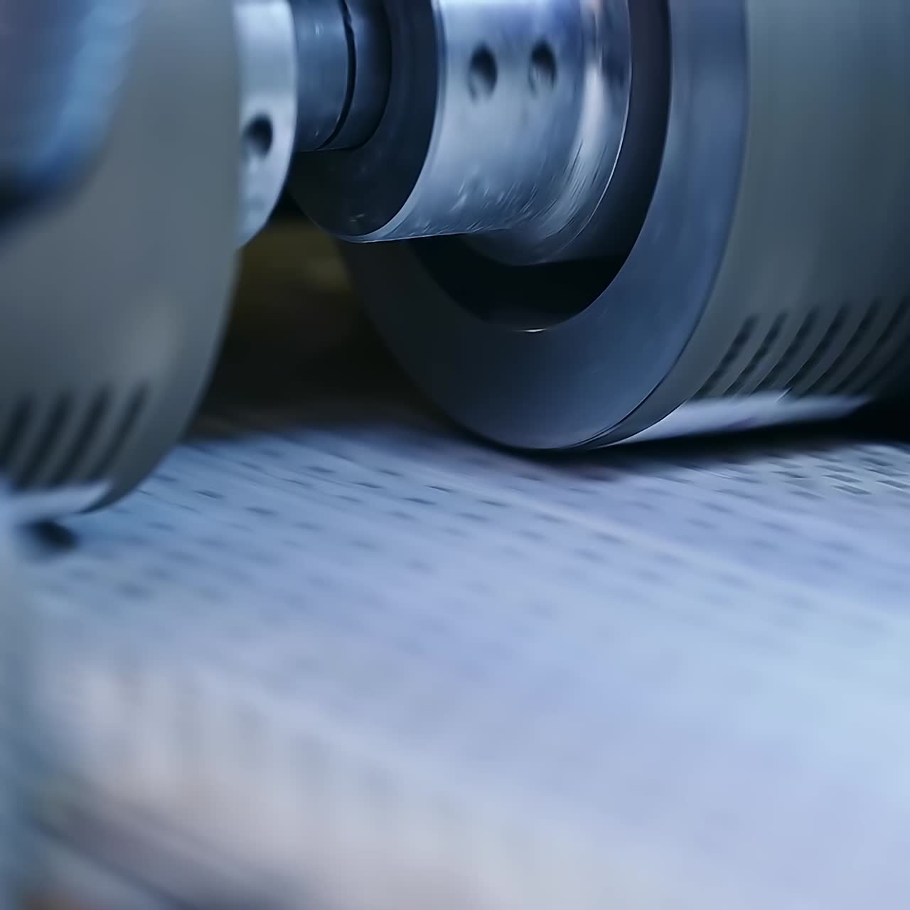 White non-woven cloth moving rapidly under the large roller. Fast conveyor belt at the diaper factory. Close up