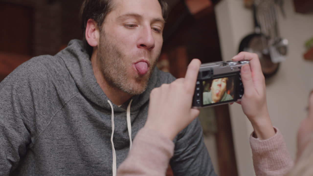 행복한 젊은 커플이 카메라를 사용하여 함께 사진을 찍고 소파에서 집에서 재미있게 로맨틱한 관계를 즐기며 서로 사진을 찍고 얼굴을 짓고 있습니다.