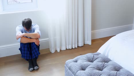 Tense-man-sitting-on-wooden-floor-in-bedroom-4k