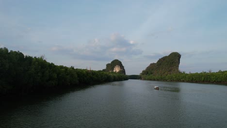 drone aéreo volando bajo a lo largo de un río y un bosque de manglares acercándose a un bote de cola larga tailandés y rocas de montaña de piedra caliza en la distancia en la ciudad de krabi tailandia