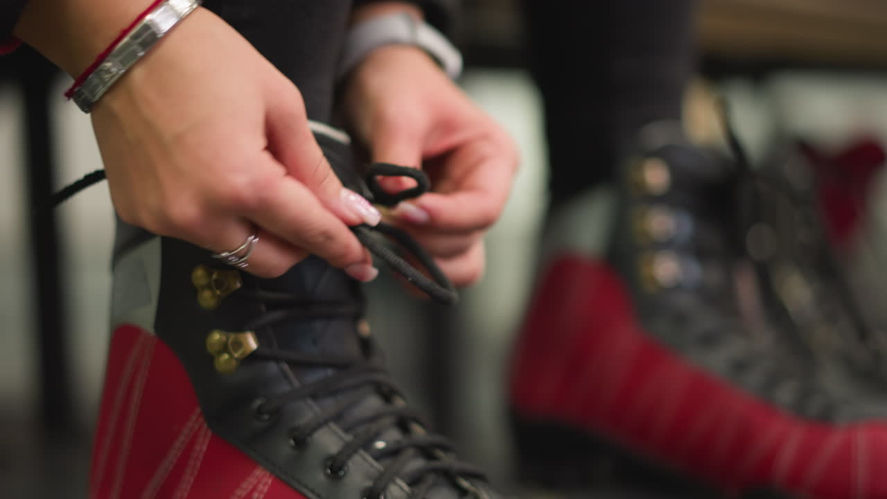 Lady putting on red black ice skates tying laces with focus on hands close up detail preparation for skating activity showing precision and strength before entering ice arena with winter sports atmosphere
