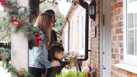 family being greeted by grandparents as they arrive for visit on christmas day with gifts