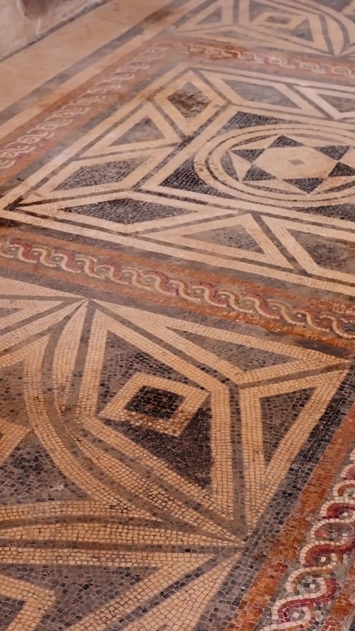 Vertical close-up of an ancient Pompeii mosaic floor with geometric Roman patterns, tiny tesserae tiles, curved lines, diamonds, and worn decorative details.