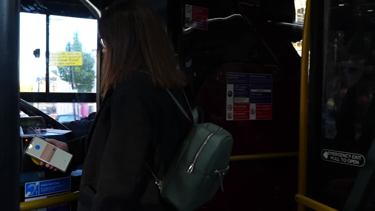 People board bus, tapping phones for contactless payment during evening commute in London