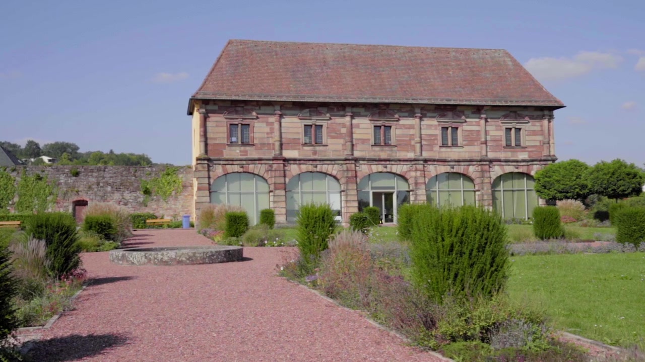 Ripresa cinematografica al rallentatore dell'Orangerie di Blieskastel in estate. Cattura la bellezza dell'architettura tradizionale circondata da una vegetazione lussureggiante e vivaci sentieri da giardino.