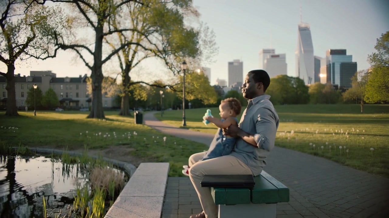 Approaching park bench dad in shirt placing briefcase seating toddler with sippy cup to watch pond