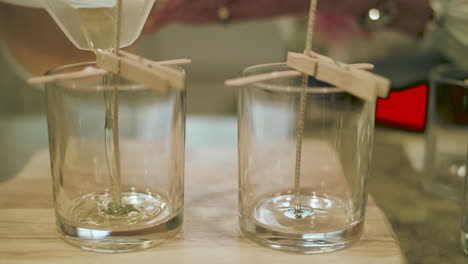 Close-up-of-hot-wax-pouring-in-slow-motion-into-empty-candle-glass-next-to-an-empty-glass