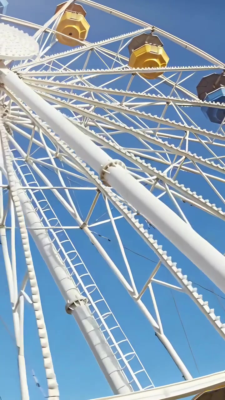 Vertical video: Tilting camera showing white Ferris wheel at fairground, exposing colorful gondolas