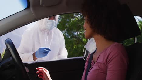 African-american-woman,-having-covid-test-done-while-sitting-in-car-by-medical-worker-outdoors