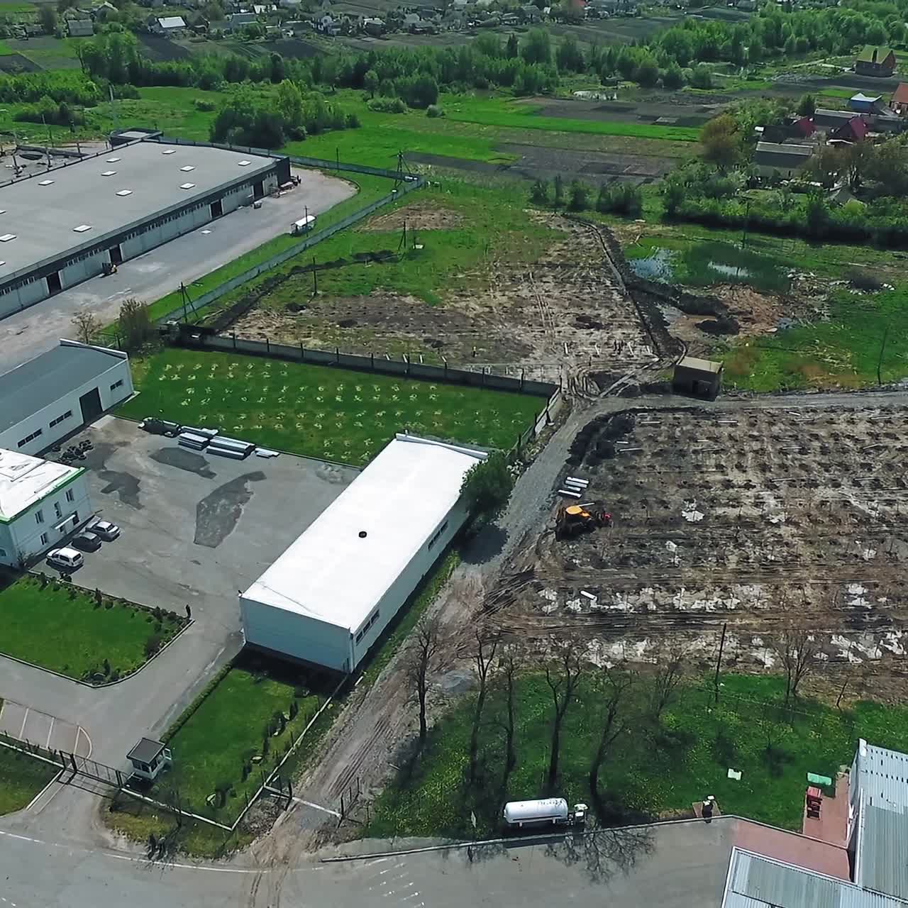 Construction ground for future solar renewable station. Industrial area and village lit with sun at backdrop. Aerial view